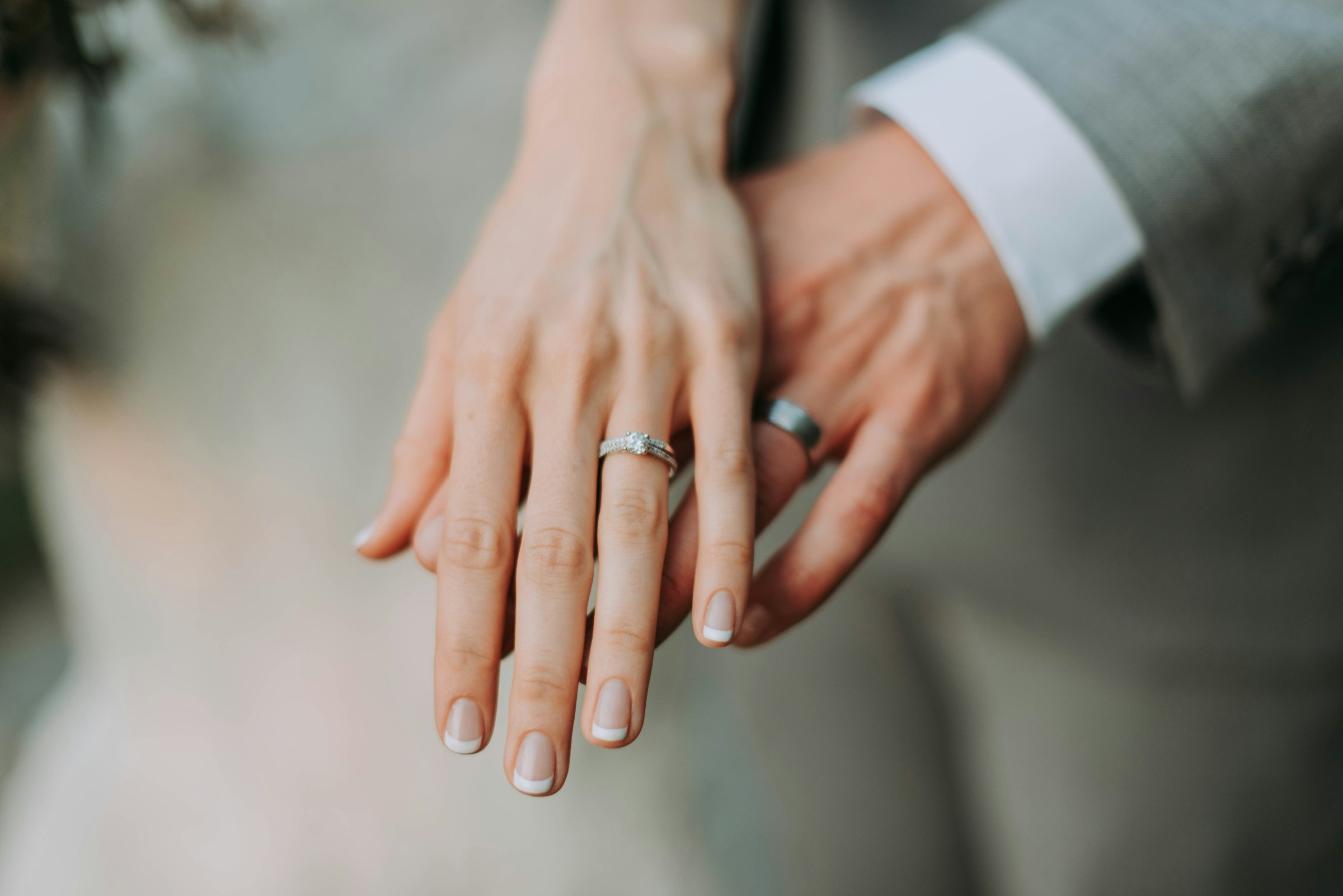 A bride's hand with her wedding ring resting on the groom's hand