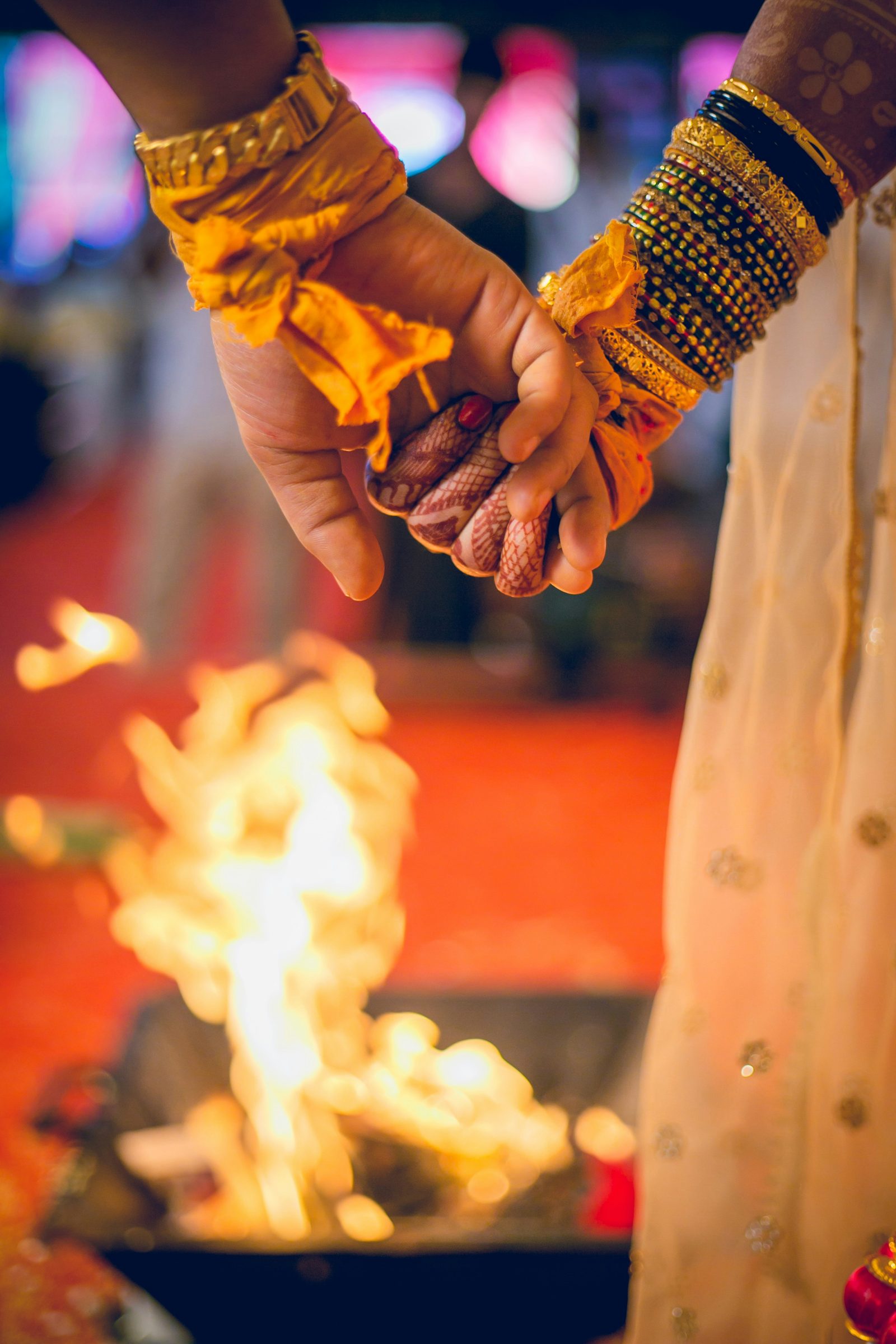The couple's joined hands, gold bangles on the bride's wrist, in front of the sacred fire