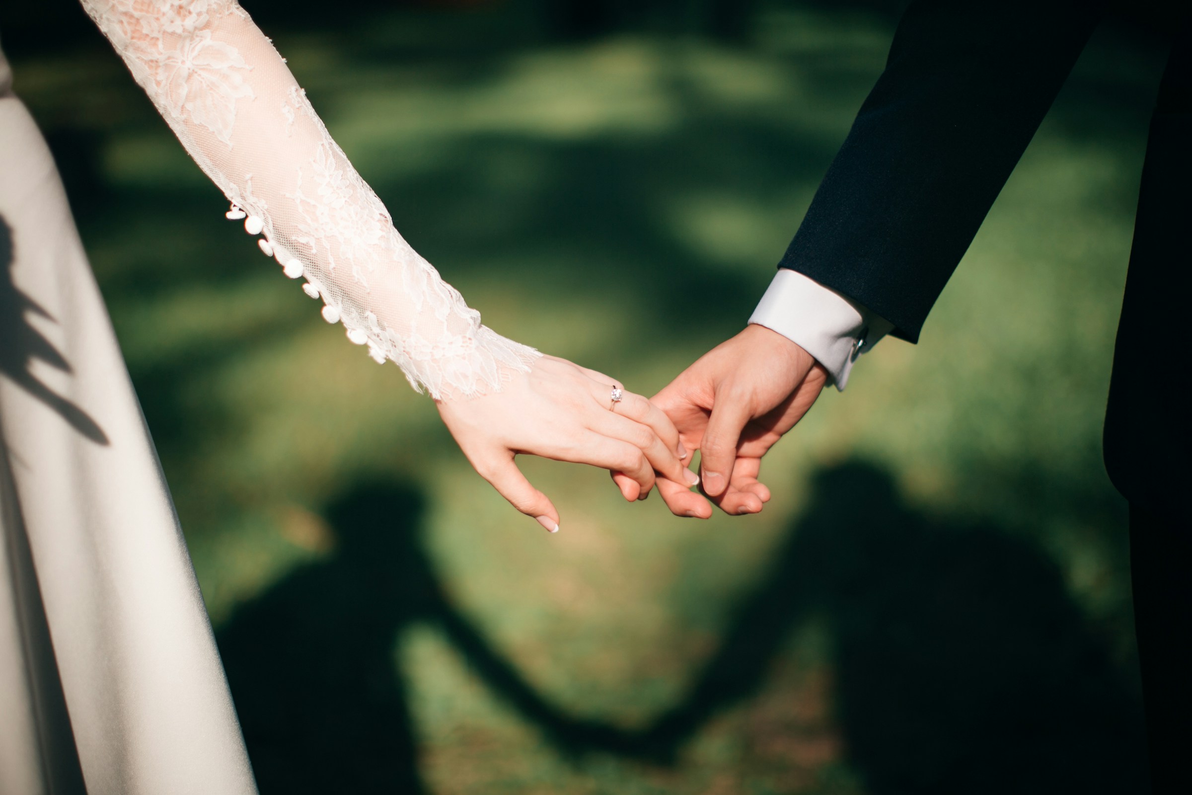 A couple holding hands, their shadows on the grass
