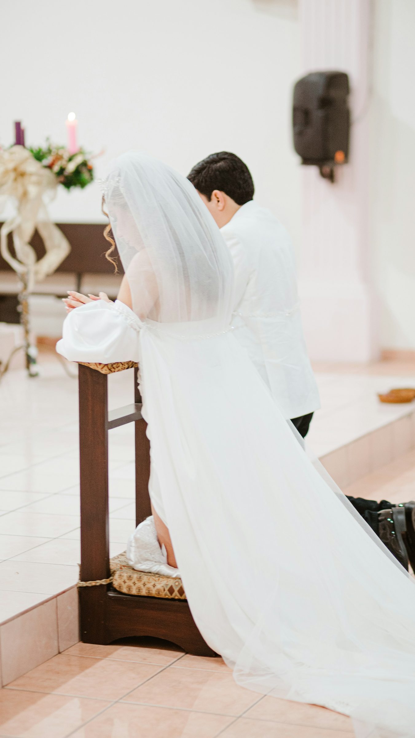 A bride and groom kneeling at the altar of a white chapel